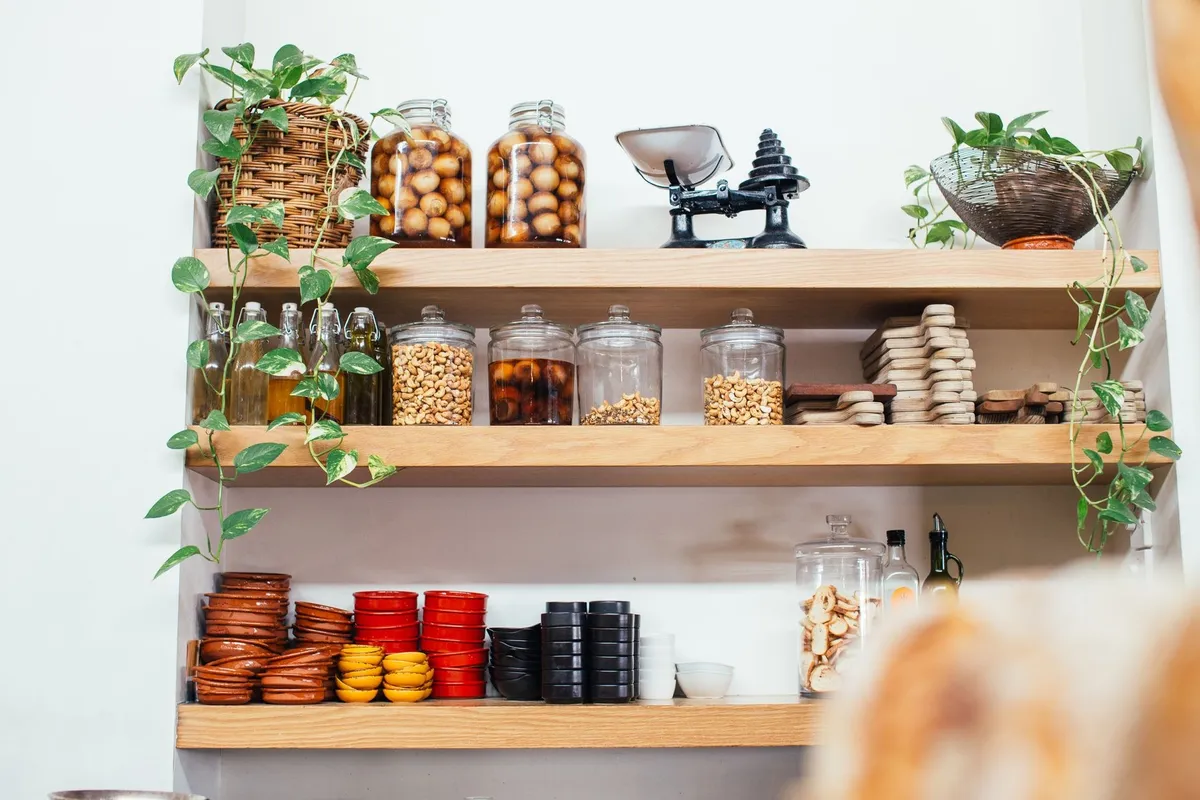 Timber shelves display glass jars filled with nuts alongside green plants and plastic containers for organization.