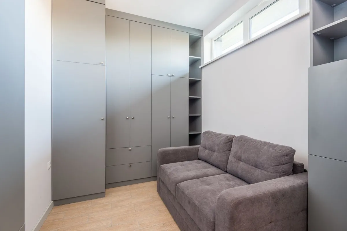 A modern apartment interior with a grey wardrobe and sofa, showcasing effective space-saving design.